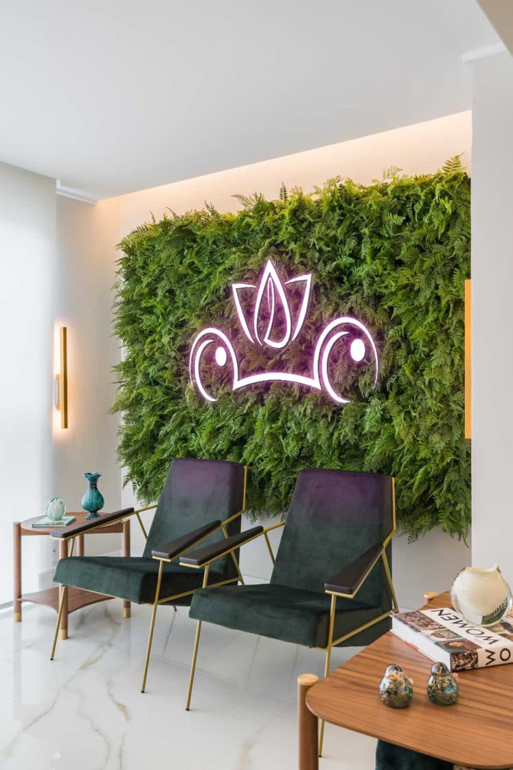 Ambiente da Liftam com parede de folhagem viva e o logo em neon rosé